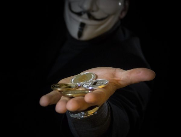 Bitcoin Kurs Prognose Bitcoin Münze auf Hand eines Mann mit einer Anonymous Maske